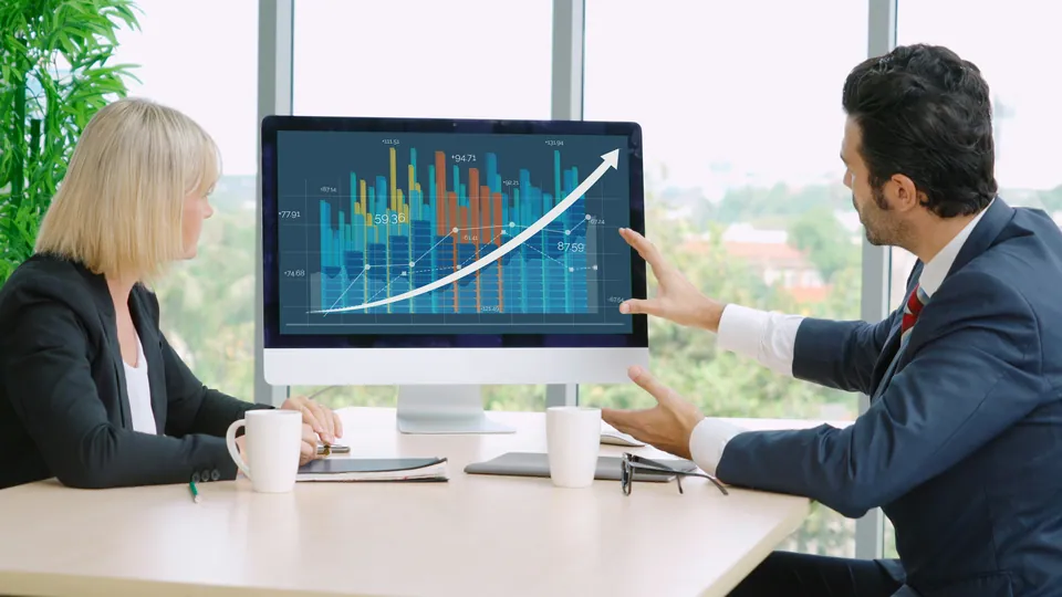 Two colleagues reviewing a rising growth chart on a desktop monitor