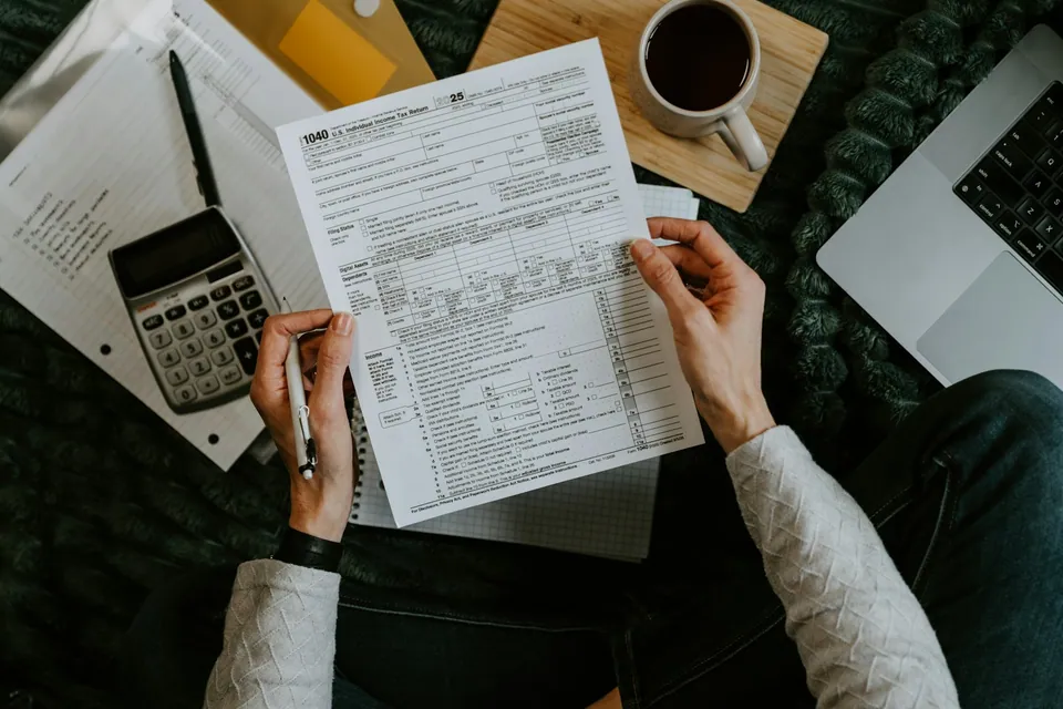 Person filling out a tax form beside a calculator, coffee and laptop