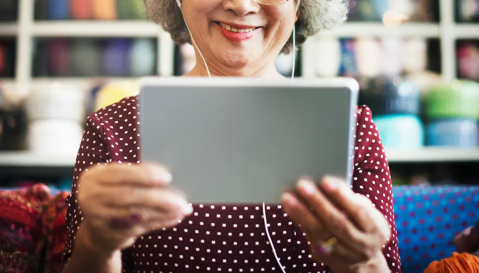 Smiling older woman with earphones holding a tablet