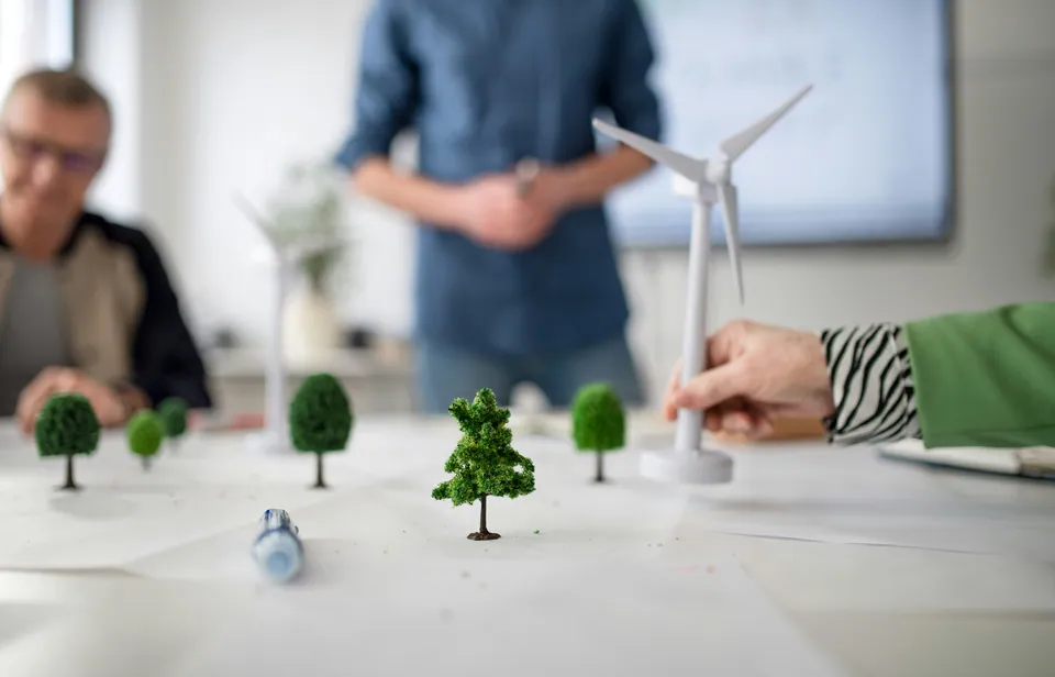 Team discussing a tabletop model with a wind turbine and miniature trees