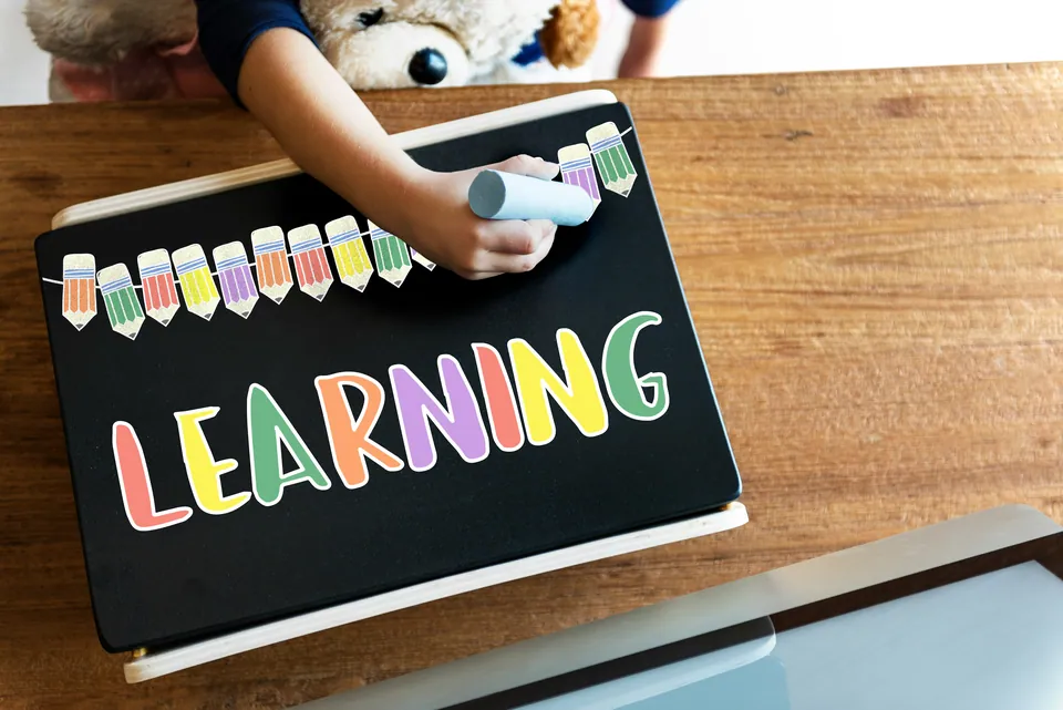 Child coloring the word LEARNING in bright letters on a chalkboard