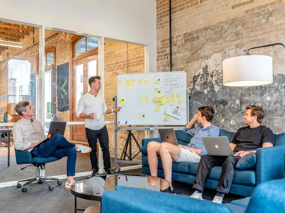 Small team meeting on sofas in a loft office with a whiteboard of sticky notes