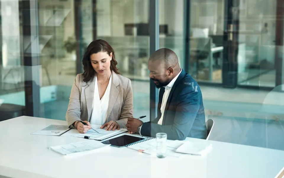 Two professionals reviewing documents at a glass conference table