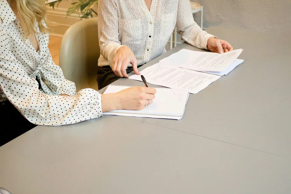 Two people signing paperwork at a gray table