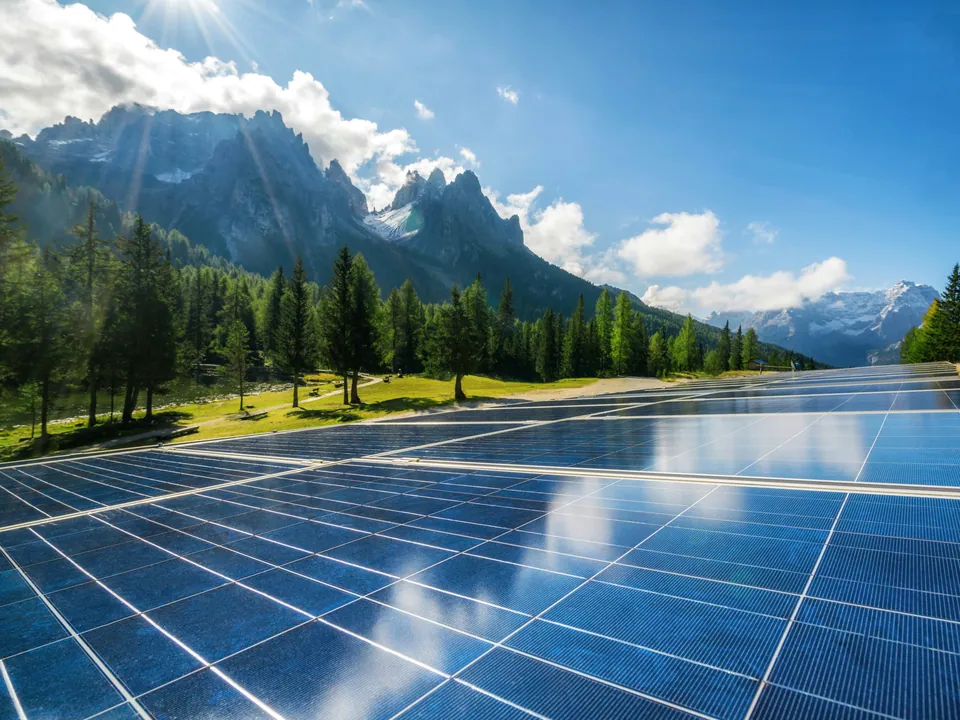 Solar panels in a meadow below forested mountain peaks