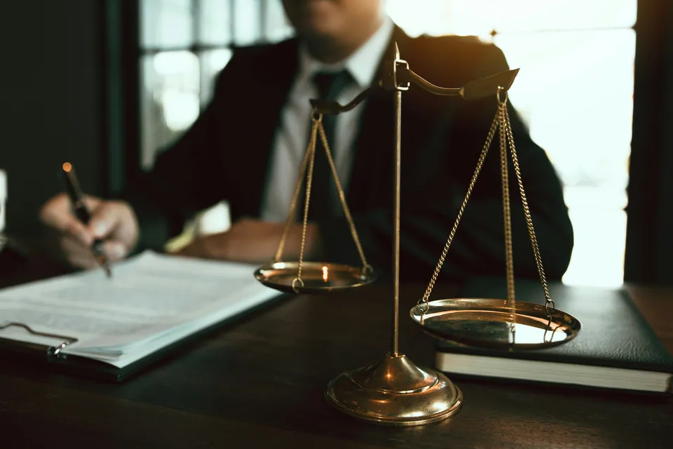 Lawyer signing a document beside a brass scale of justice