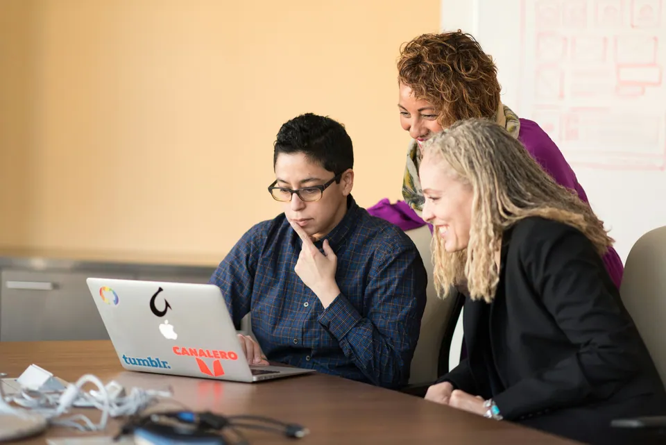 Three colleagues looking at a laptop together at a conference table