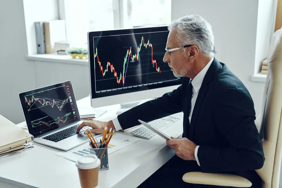 Senior trader analyzing candlestick charts on two screens
