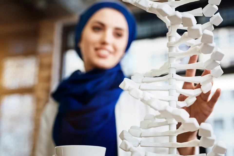 Smiling scientist reaching toward a white DNA double helix model