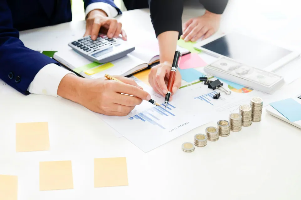 Team reviewing charts with a calculator and stacked coins on a desk