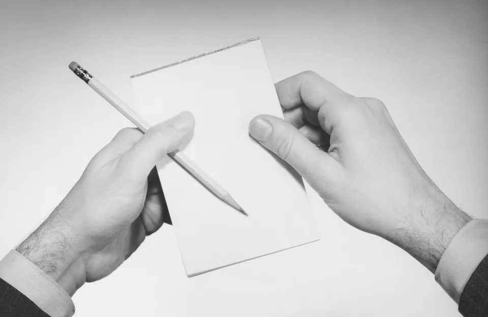 Black and white photo of hands holding a pencil and a blank note card