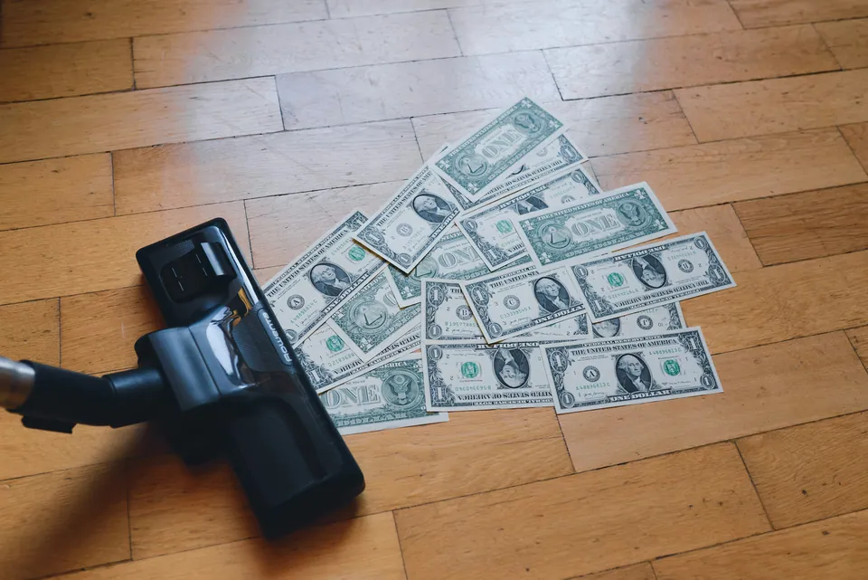 Vacuum cleaner nozzle next to scattered dollar bills on a wooden floor