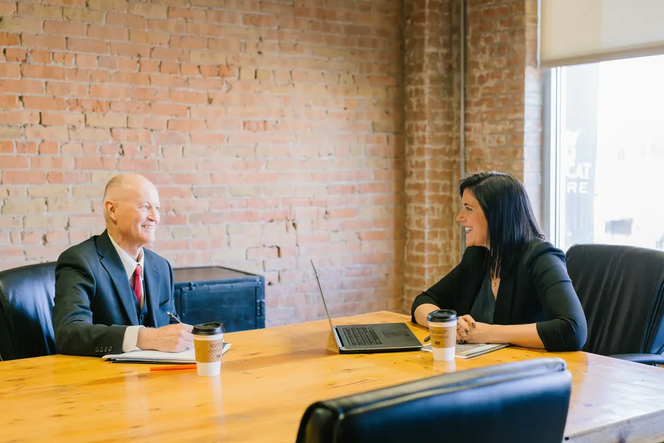 Two colleagues talking across a wooden table in a brick-walled office