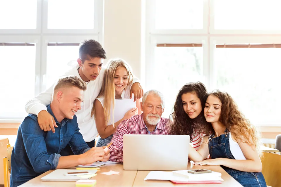 Grandfather and grandchildren gathered around a laptop at a table