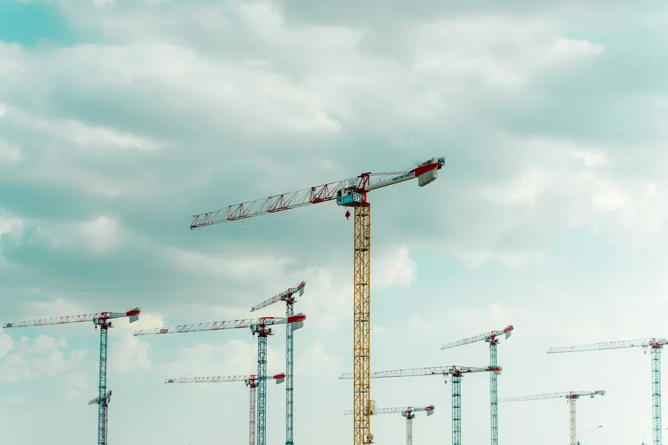 Several construction cranes against a cloudy sky