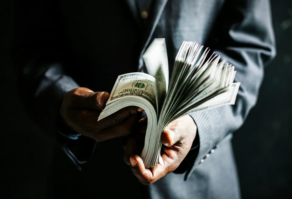 Person in a suit fanning a stack of hundred-dollar bills