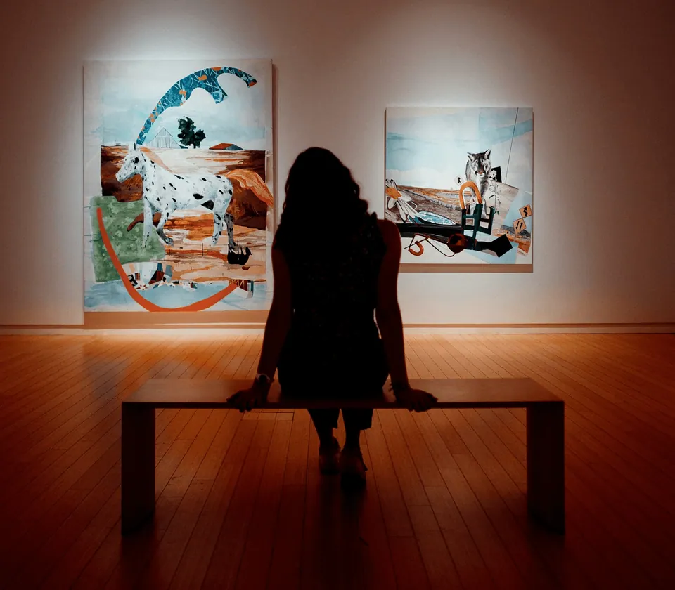 Visitor sitting on a bench in front of paintings in a gallery