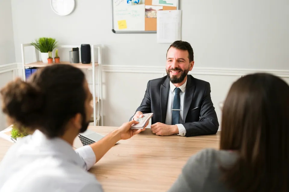 Smiling manager handing a document to a couple across a desk