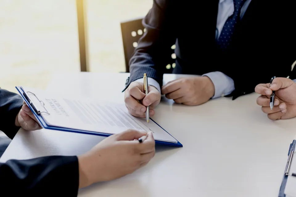 Two people signing documents on a clipboard at a white table