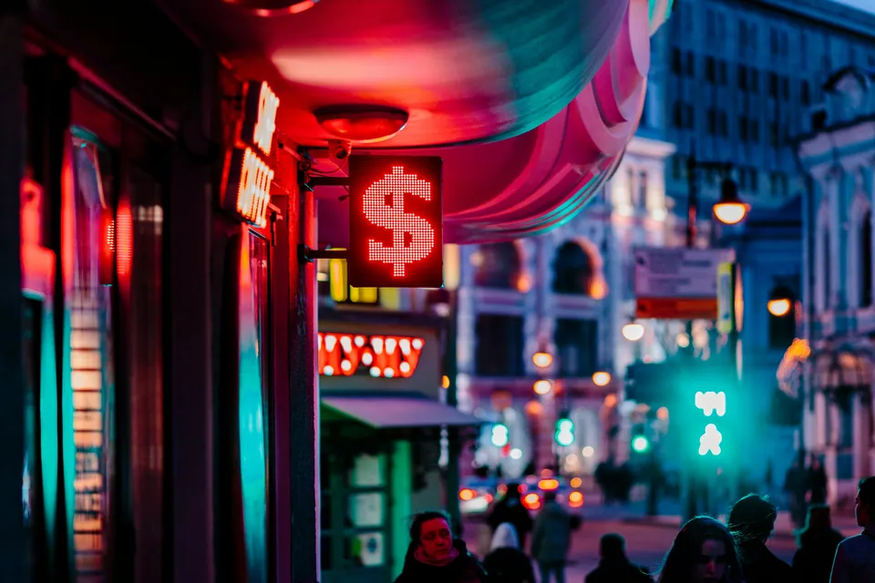 Neon dollar sign glowing above a busy city street at night