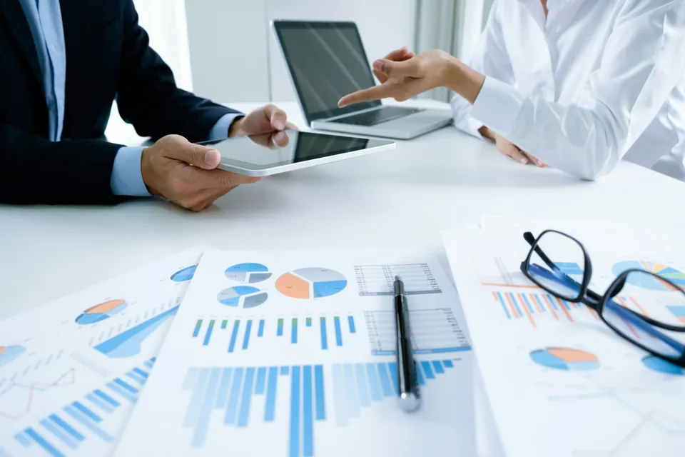 Colleagues with tablets over printed charts and reports
