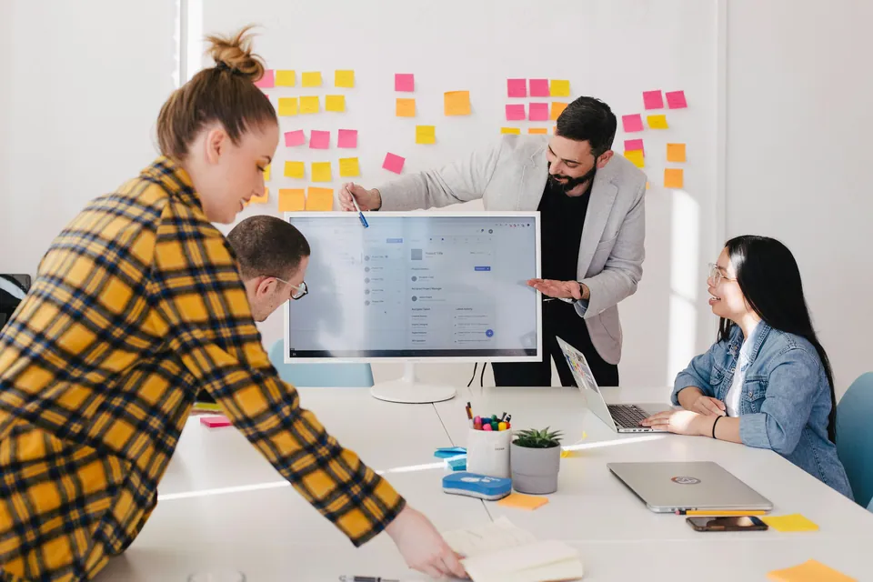 Team gathered around a monitor in front of a wall of sticky notes