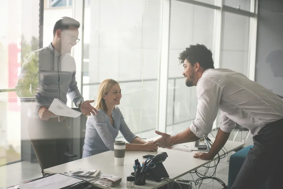Colleagues shaking hands across a desk in a glass office