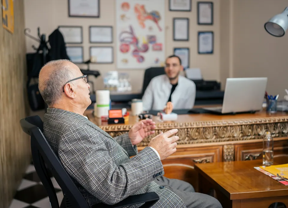 Older man in a tweed jacket meeting an advisor at a wooden desk