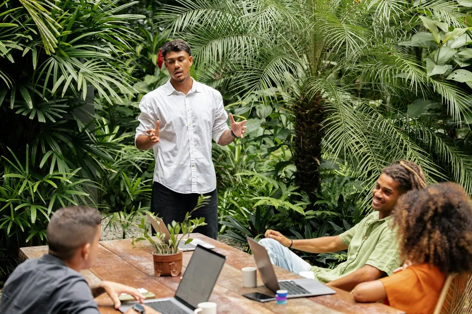 Founder pitching to a small team at an outdoor table among palms