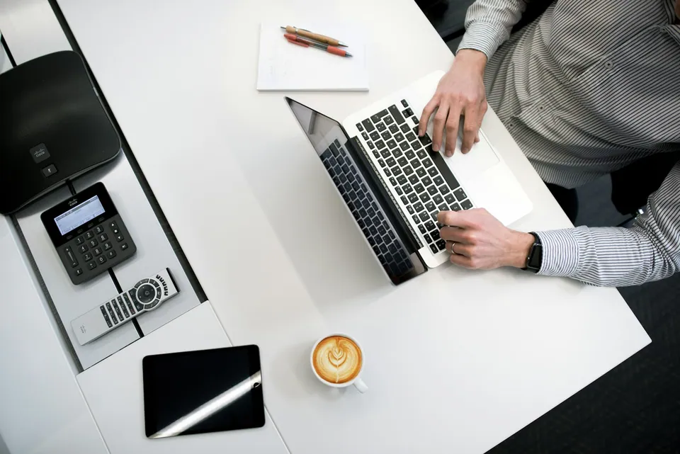 Overhead view of hands typing on a laptop beside a card reader and coffee