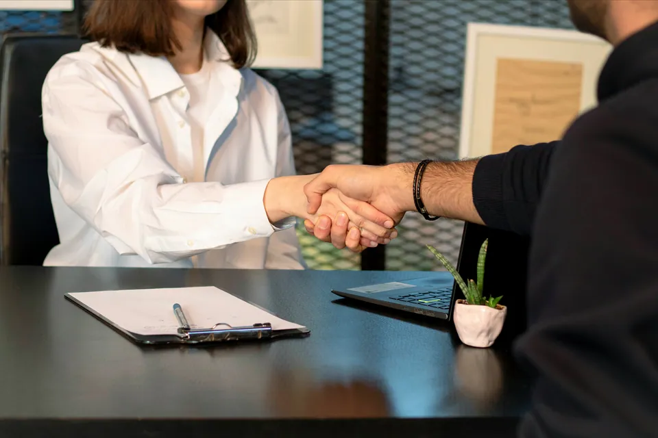 Two people shaking hands over a desk with a clipboard