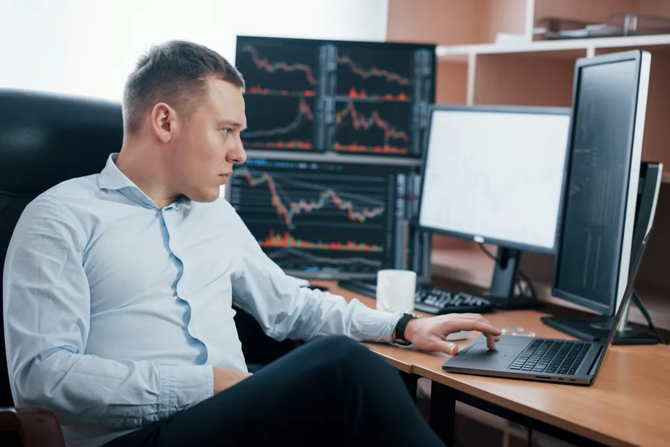 Analyst at a desk with multiple monitors showing market charts