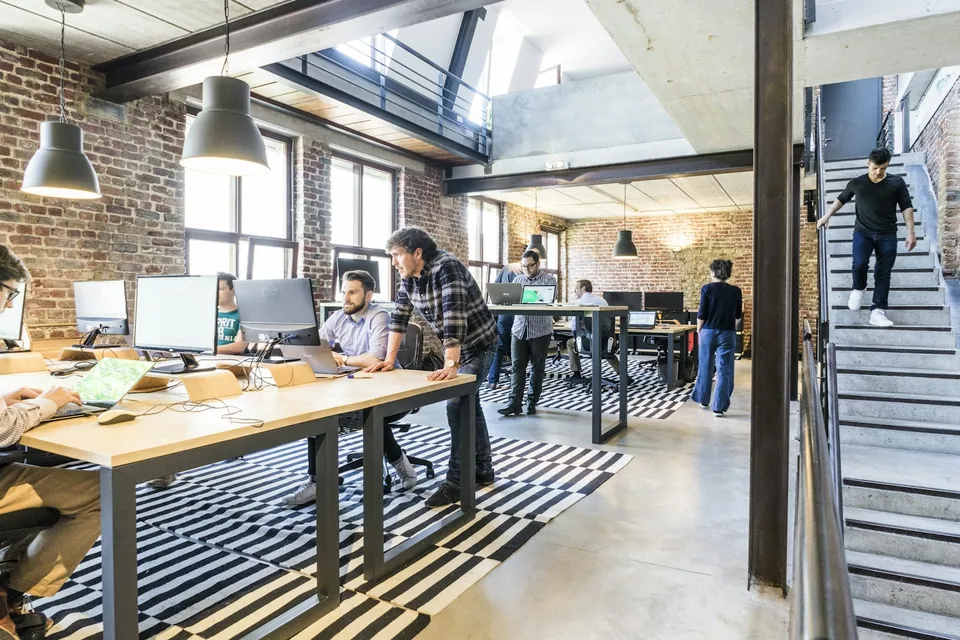 Busy open-plan loft office with desks and an industrial staircase