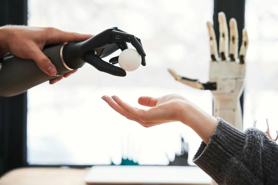Robotic prosthetic hand passing a white ball to a human hand