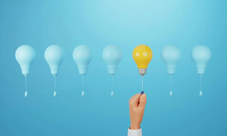 Hand holding a lit yellow light bulb among unlit blue bulbs