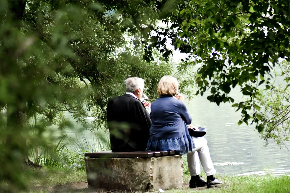 Older couple sitting on a bench by a lake under trees