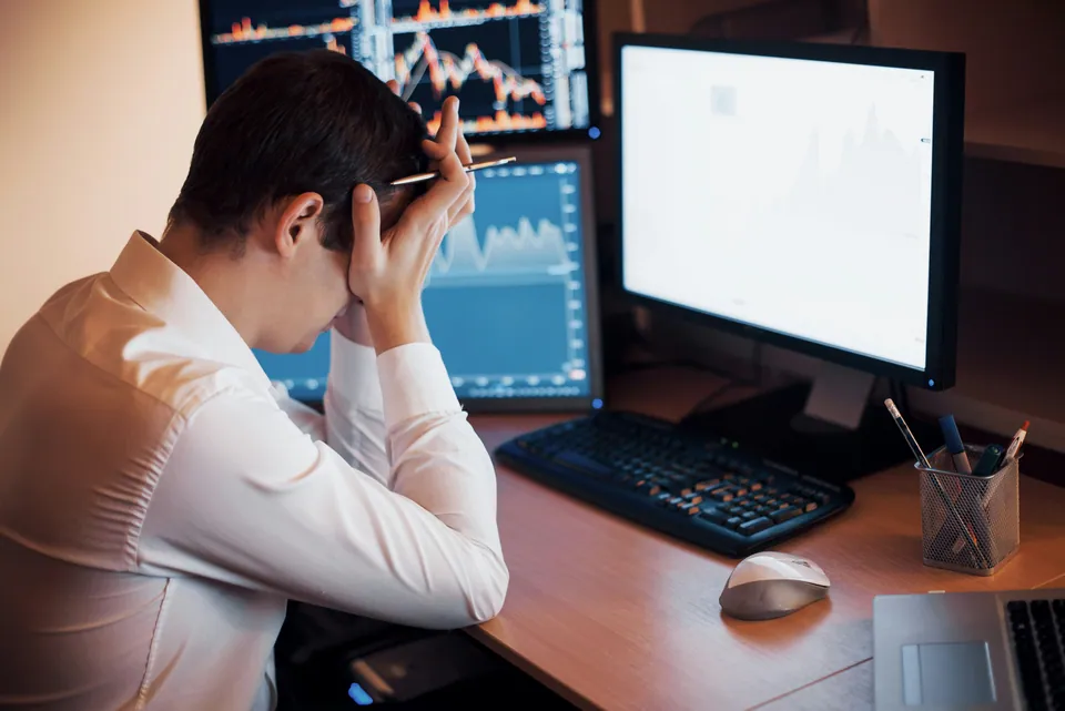 Stressed trader holding his head in front of market chart monitors