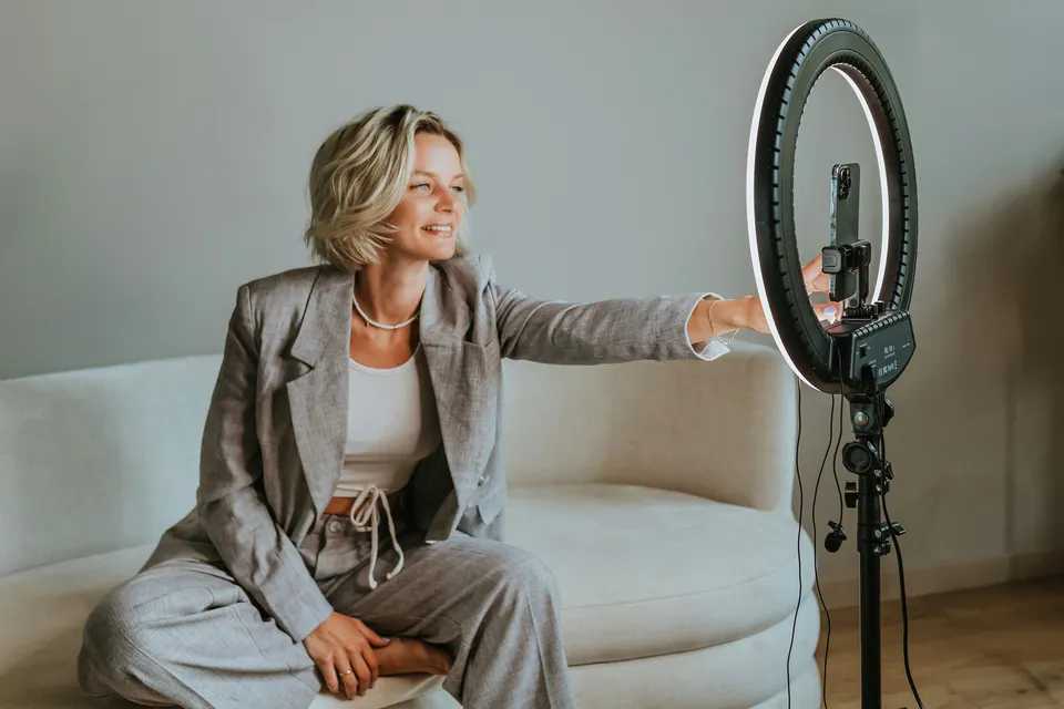 Woman in a gray suit adjusting a ring light on a sofa