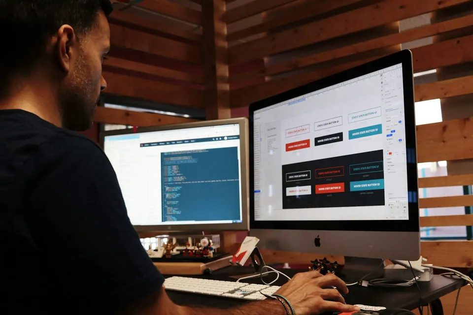 Developer working at two monitors with code and a web app
