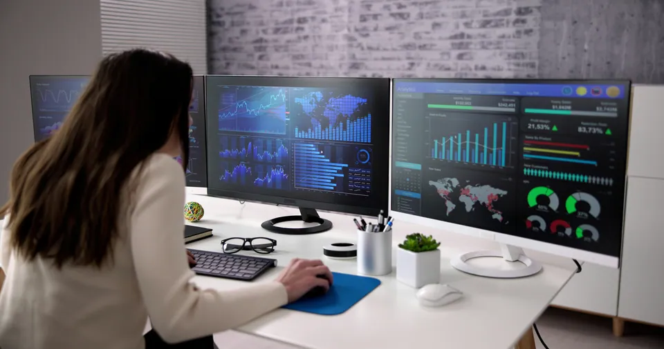 Analyst working at three monitors full of data dashboards
