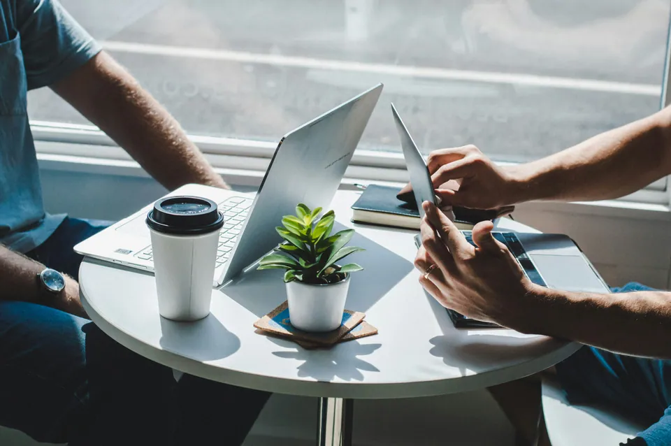 Two people working on a laptop and tablet at a small round table