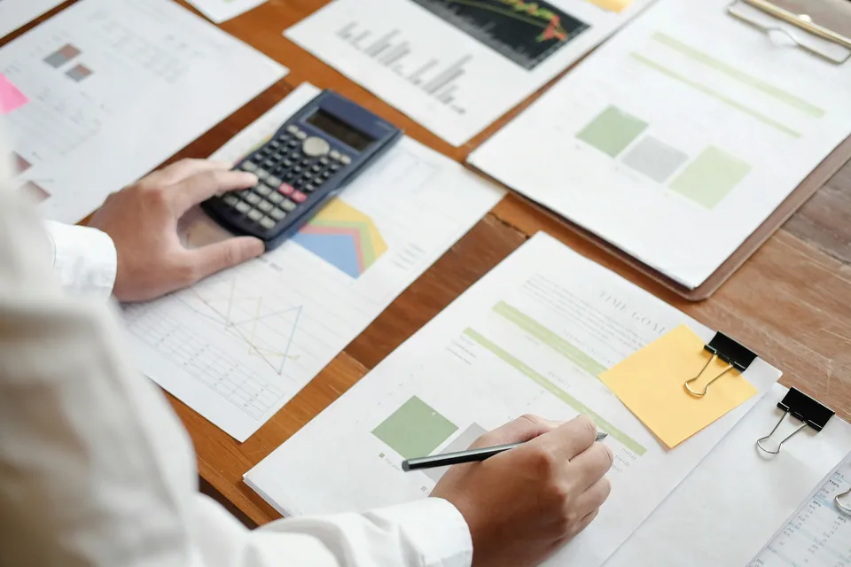 Hands using a calculator over printed charts and reports