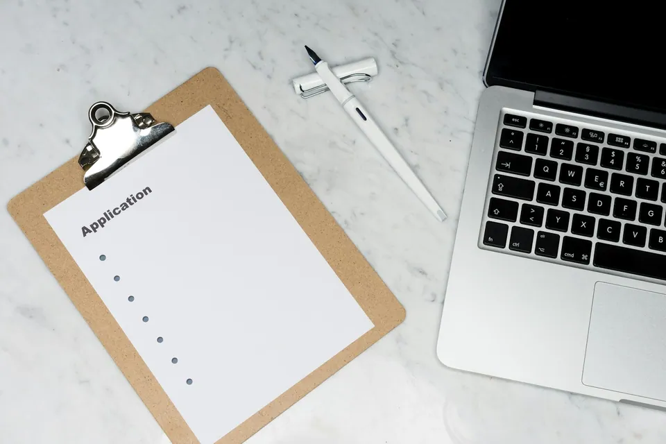 Clipboard with a blank application form next to a laptop