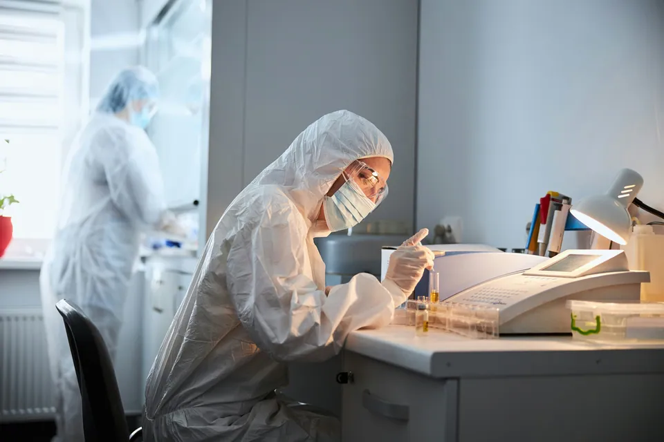 Lab scientist in protective gear working at a bench
