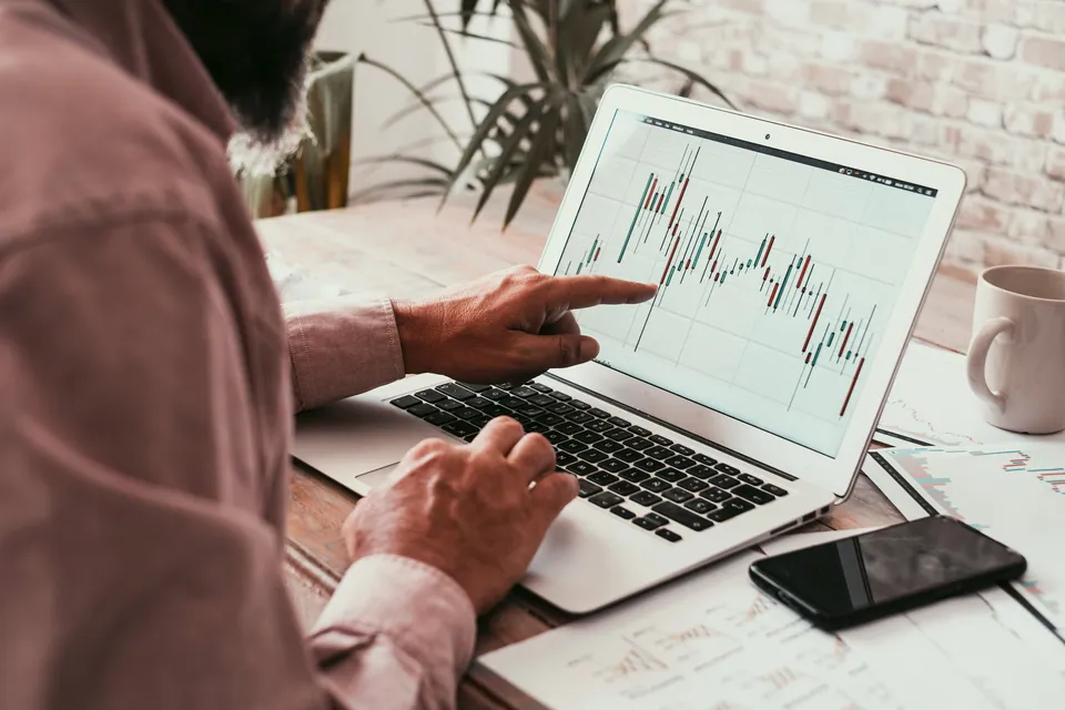 Person pointing at a candlestick chart on a laptop