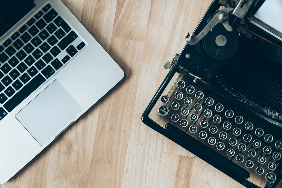 Laptop next to a vintage typewriter on a wooden desk