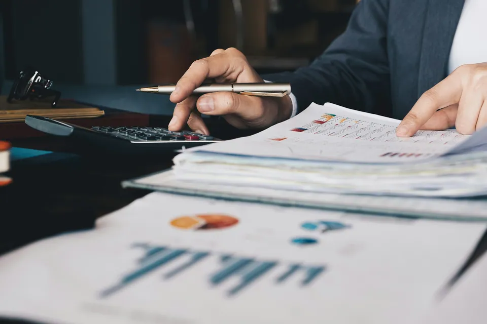 Hands with a pen and calculator over printed financial reports