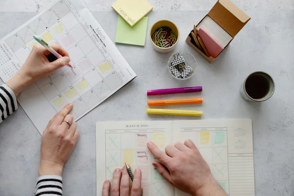 Two people planning on a paper calendar with sticky notes and markers
