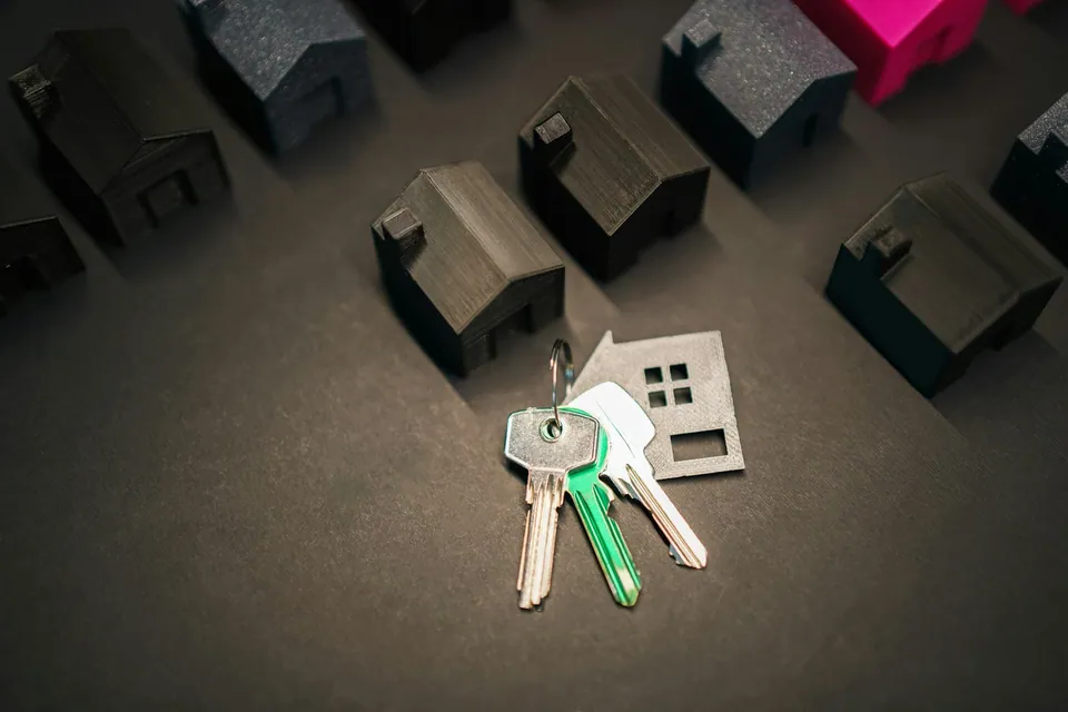 House keys beside small model houses on a dark surface