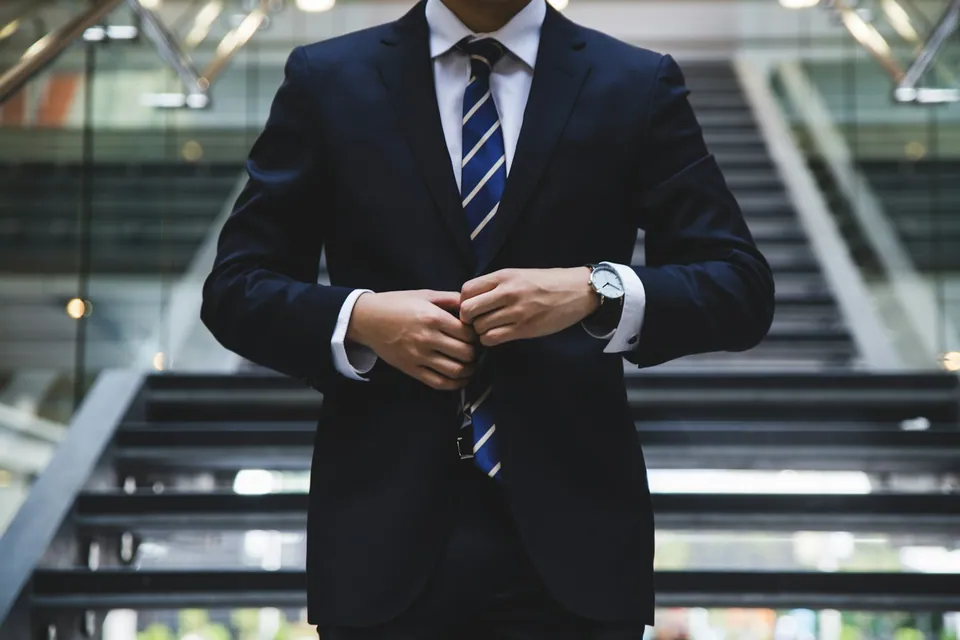 Businessman in a navy suit buttoning his jacket on a staircase